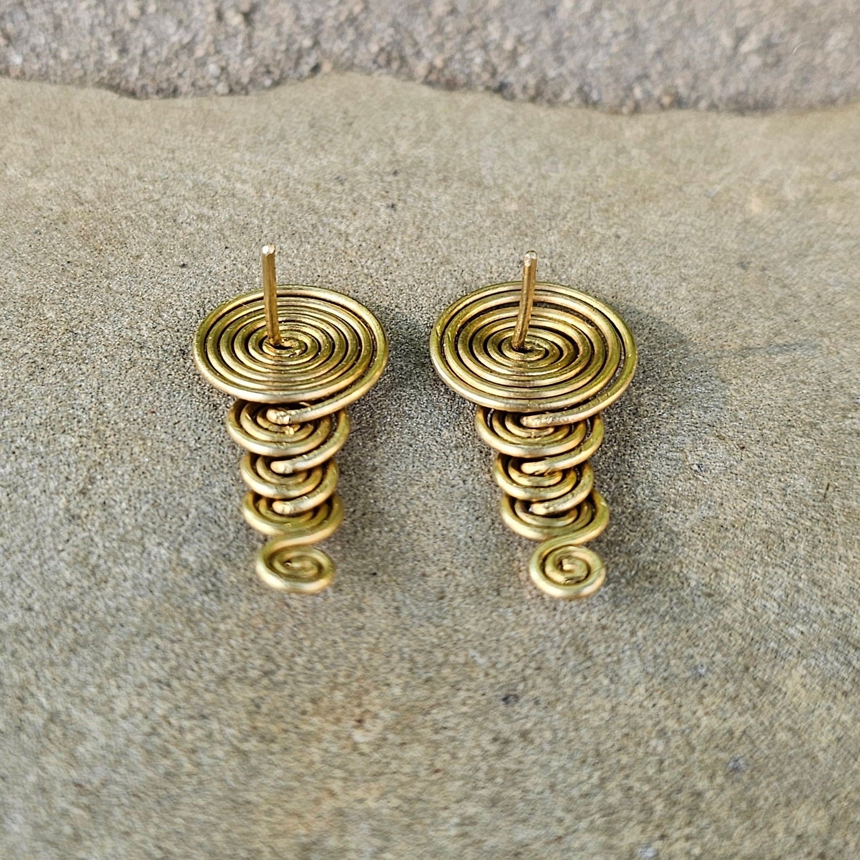 Gold spiral earrings on a stone surface. Shop Kamawe