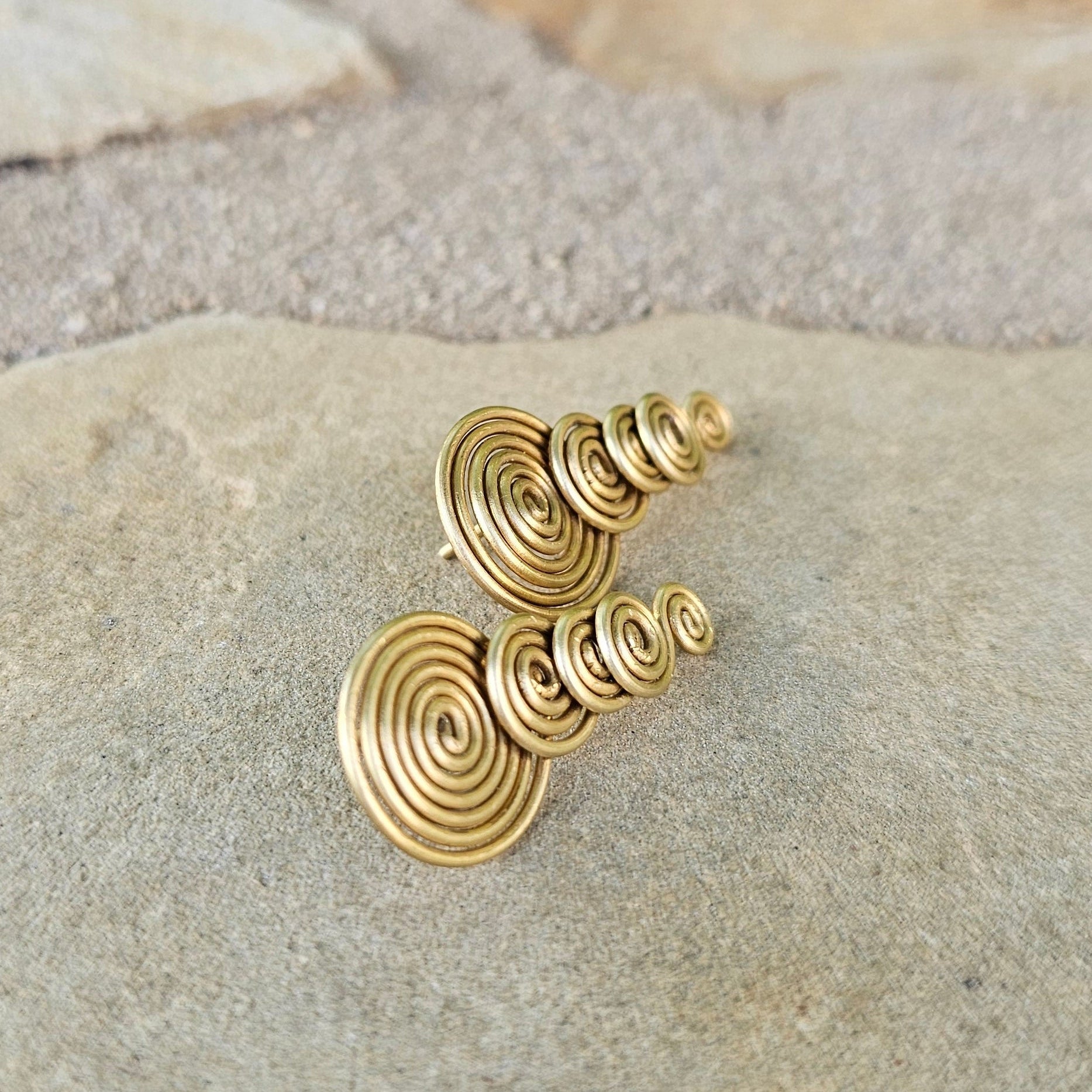 Gold spiral earrings on a stone surface. Shop Kamawe