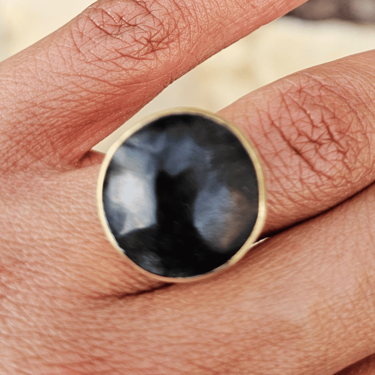A close-up of a gold ring with a large, polished black dome stone worn on a person's finger. Shop Kamawe