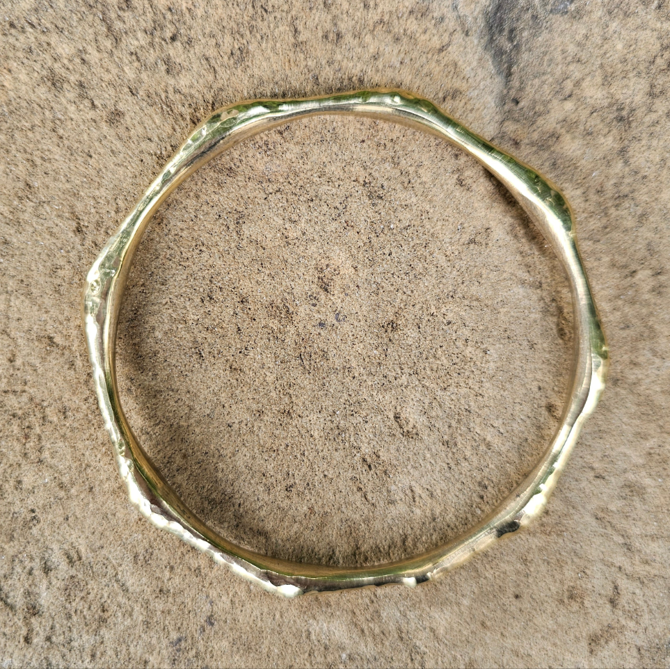 An image of gold-color Bold hammered brass bangle with wave-like texture. Shop Kamawe
