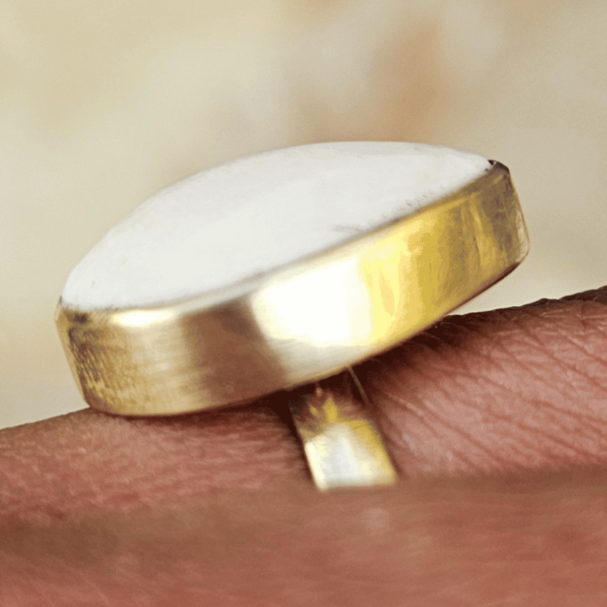 A gold ring with a large, rounded white stone, shown worn on a person's finger against a soft, blurred beige background. Shop Kamawe