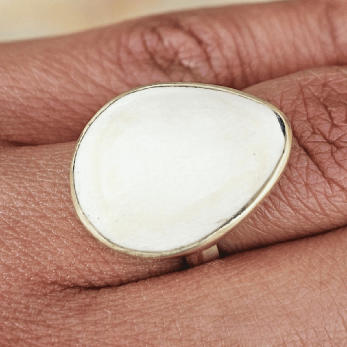 A close-up of a silver ring with a large, smooth, oval white stone set on a finger. Shop Kamawe