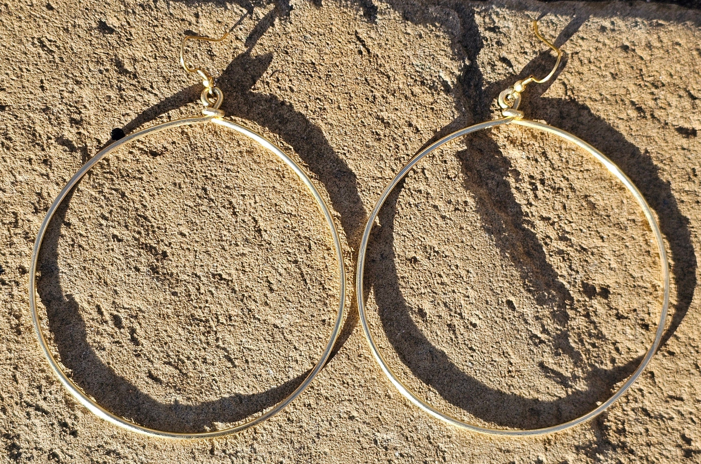 An image of gold-color Everyday mid-size polished brass hoops. Shop Kamawe