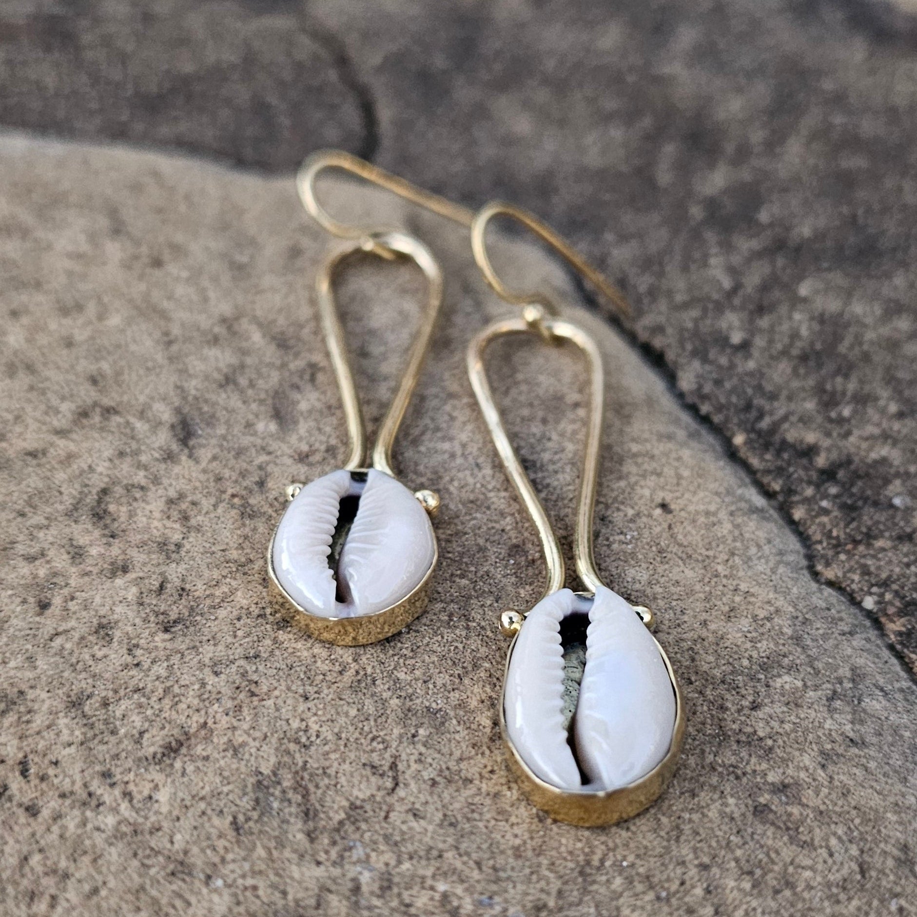 An image of gold & beige-color Brass filigree framing a single cowrie shell. Shop Kamawe