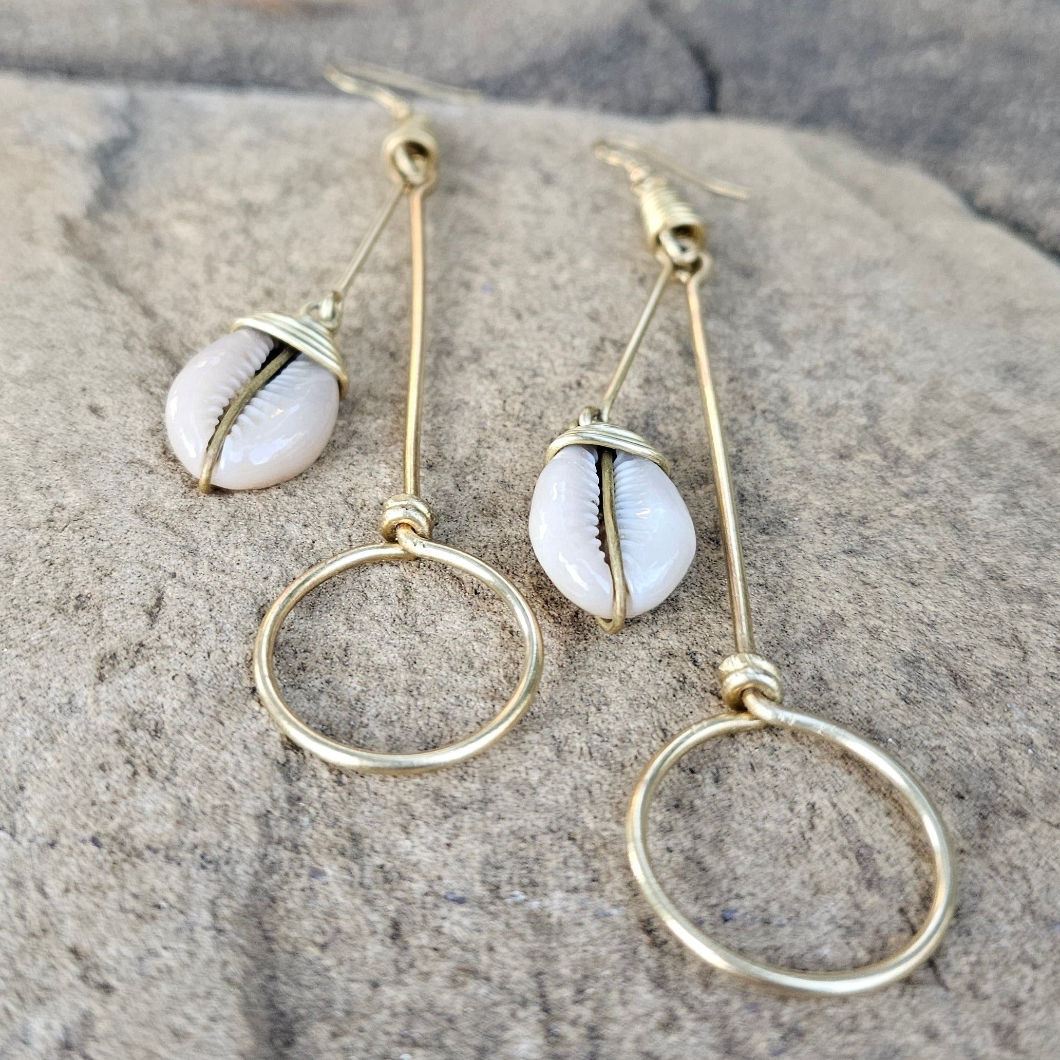 An image of gold & beige-color Thin brass hoops accented with tiny cowrie. Shop Kamawe