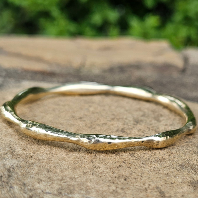An image of gold-color Compact hammered brass bangle inspired by ocean ripples. Shop Kamawe
