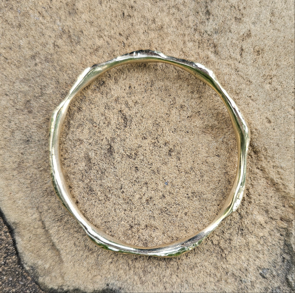 An image of gold-color Compact hammered brass bangle inspired by ocean ripples. Shop Kamawe