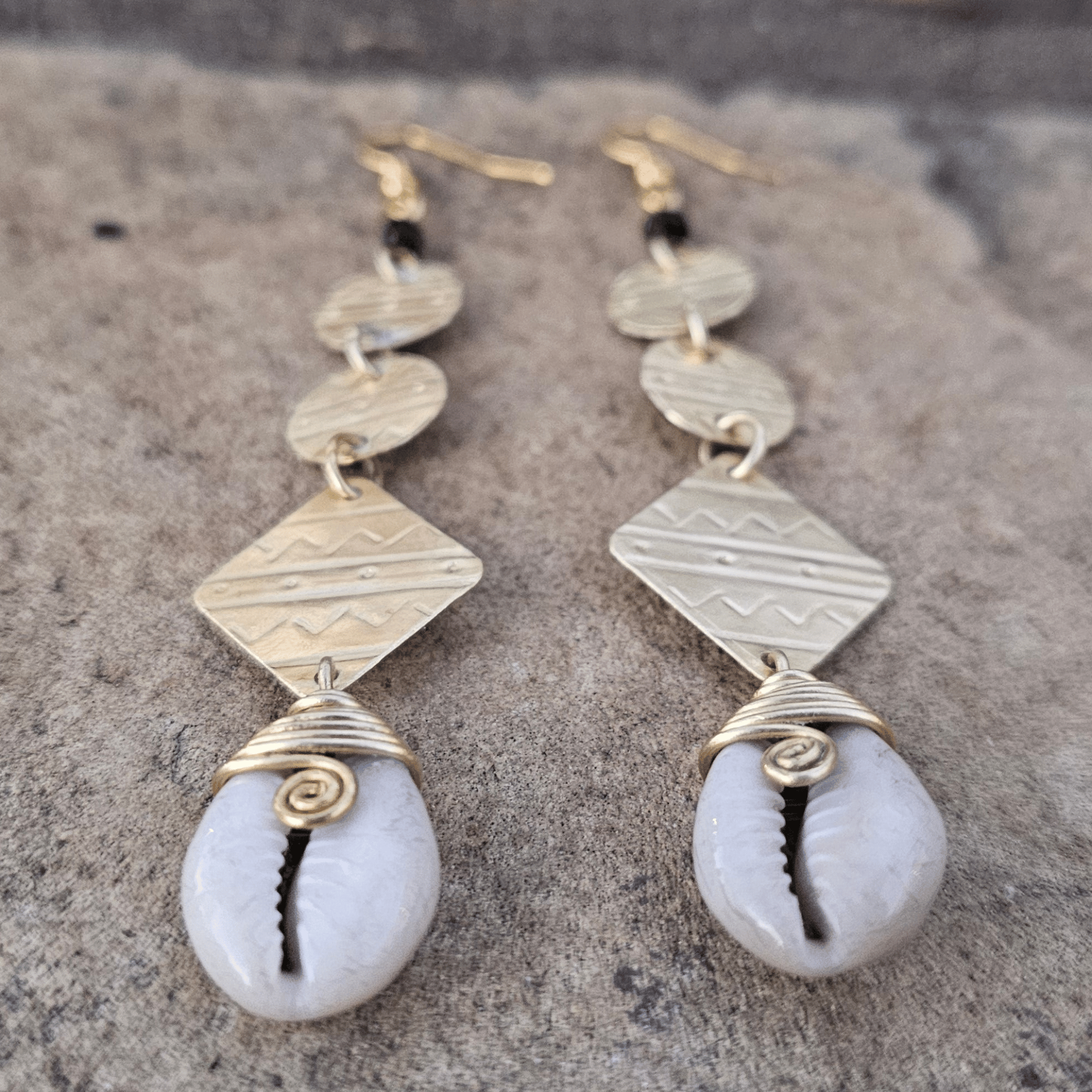 An image of gold & beige-color Statement brass drop earrings accented with authentic cowrie shells. Shop Kamawe