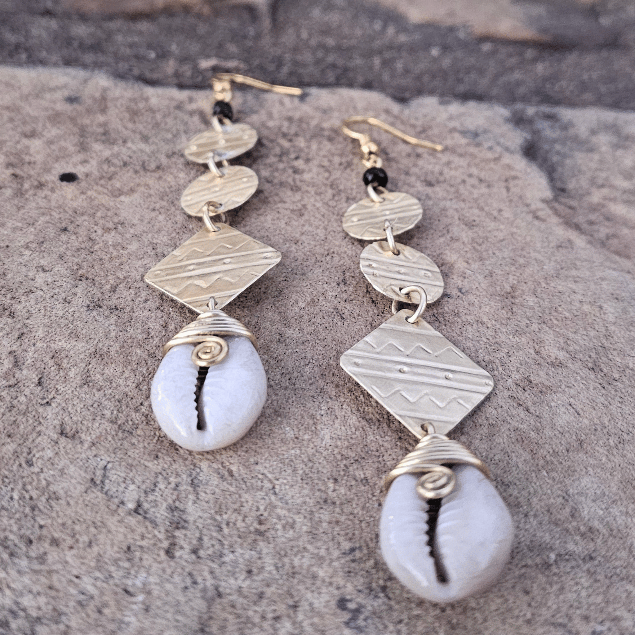 An image of gold & beige-color Statement brass drop earrings accented with authentic cowrie shells. Shop Kamawe