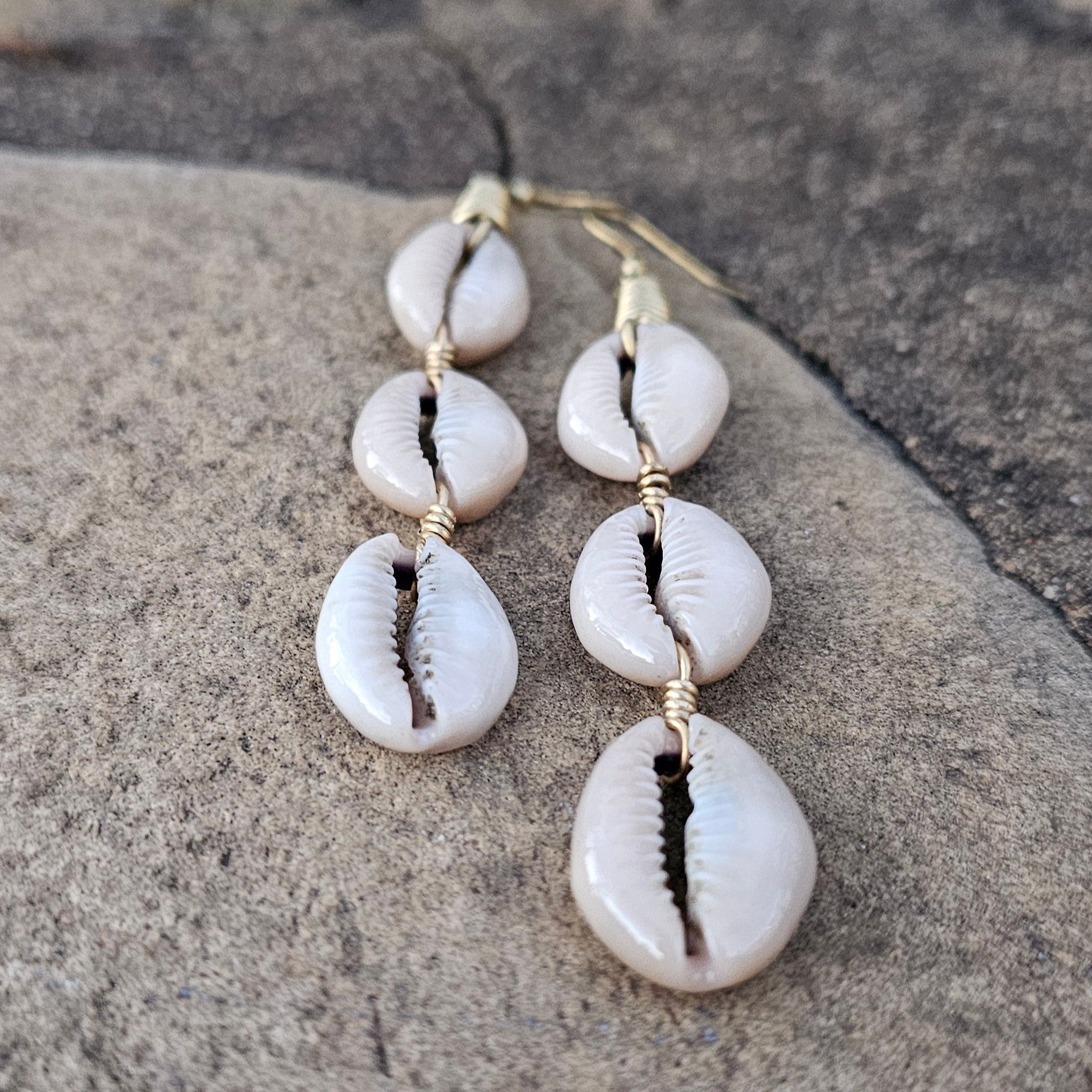 An image of gold & beige-color Three cowrie shells aligned in a sleek brass drop. Shop Kamawe