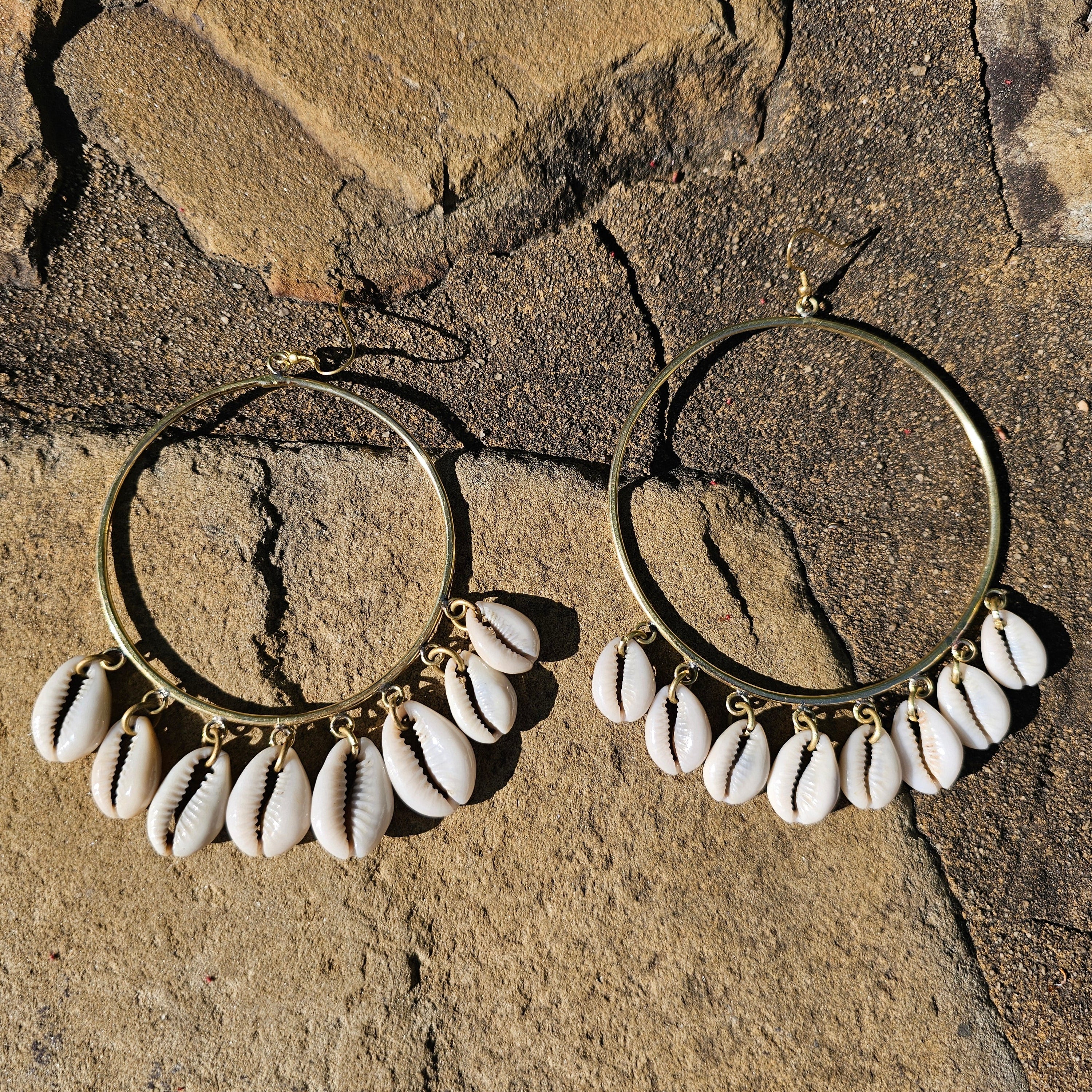 An image of gold & beige-color Big brass hoops with multiple cowrie shells falling in layers. Shop Kamawe
