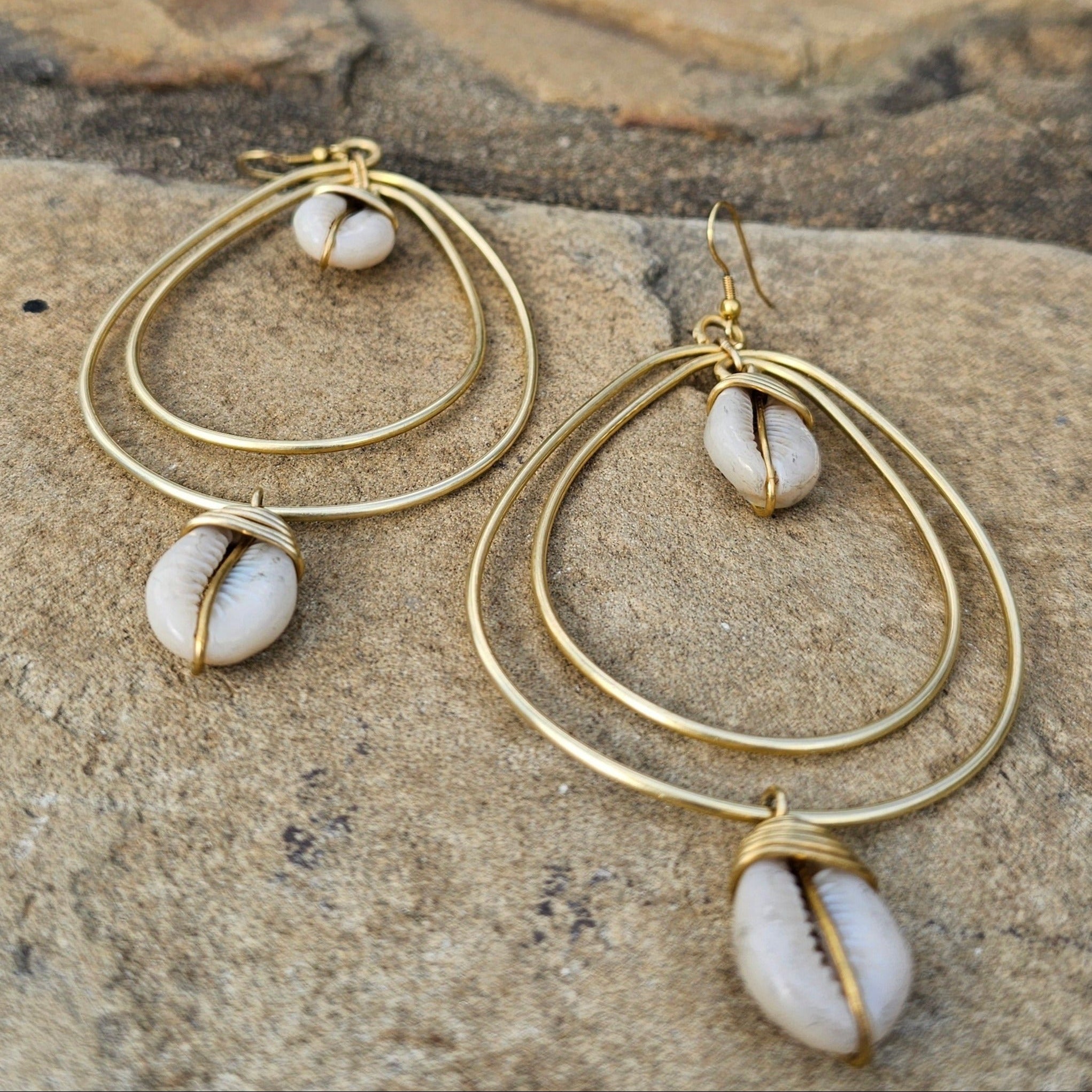 An image of gold & beige-color Teardrop brass frame cradling a single cowrie. Shop Kamawe