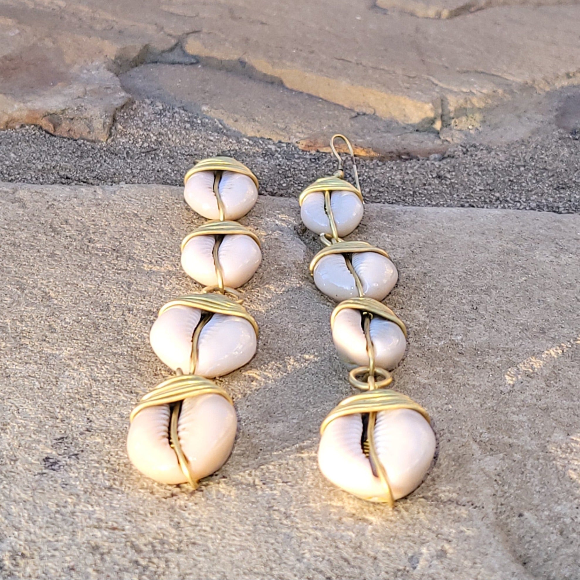 An image of gold & beige-color Straight-line brass drops finished with cowrie shells. Shop Kamawe