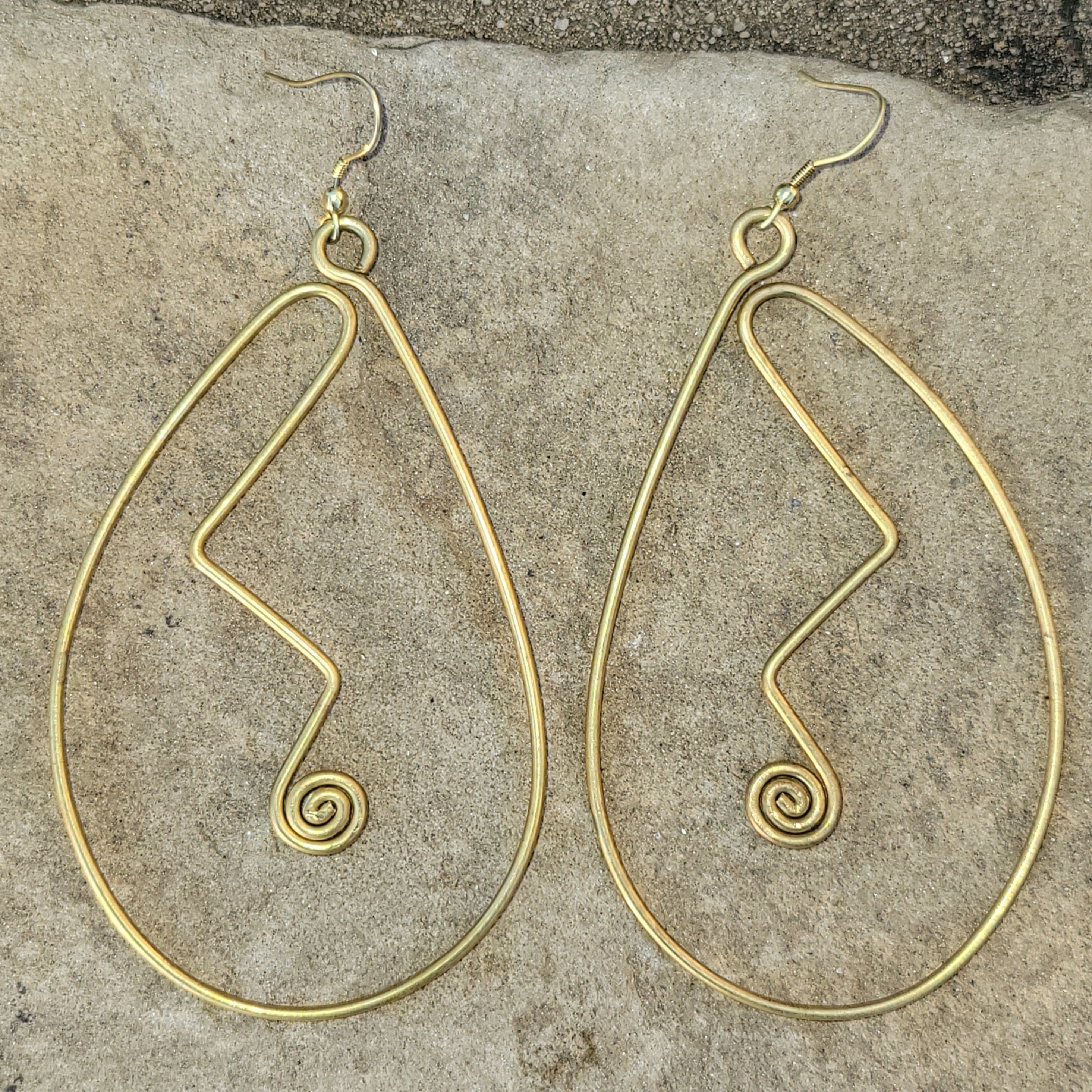 An image of gold-color Sweeping curved brass shapes that hug the line of the face. Shop Kamawe