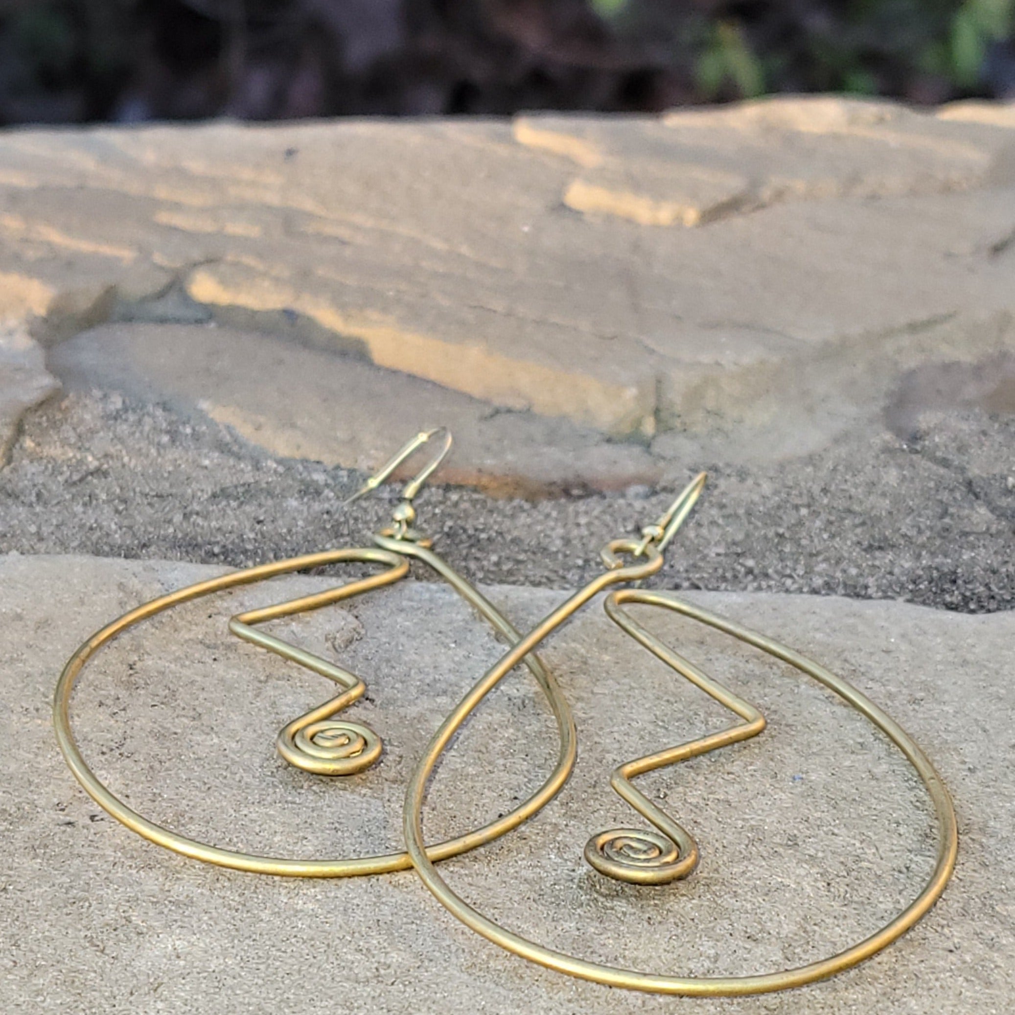 An image of gold-color Sweeping curved brass shapes that hug the line of the face. Shop Kamawe