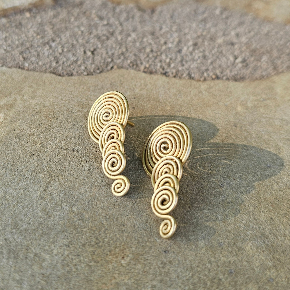 Gold spiral earrings on a stone surface. Shop Kamawe