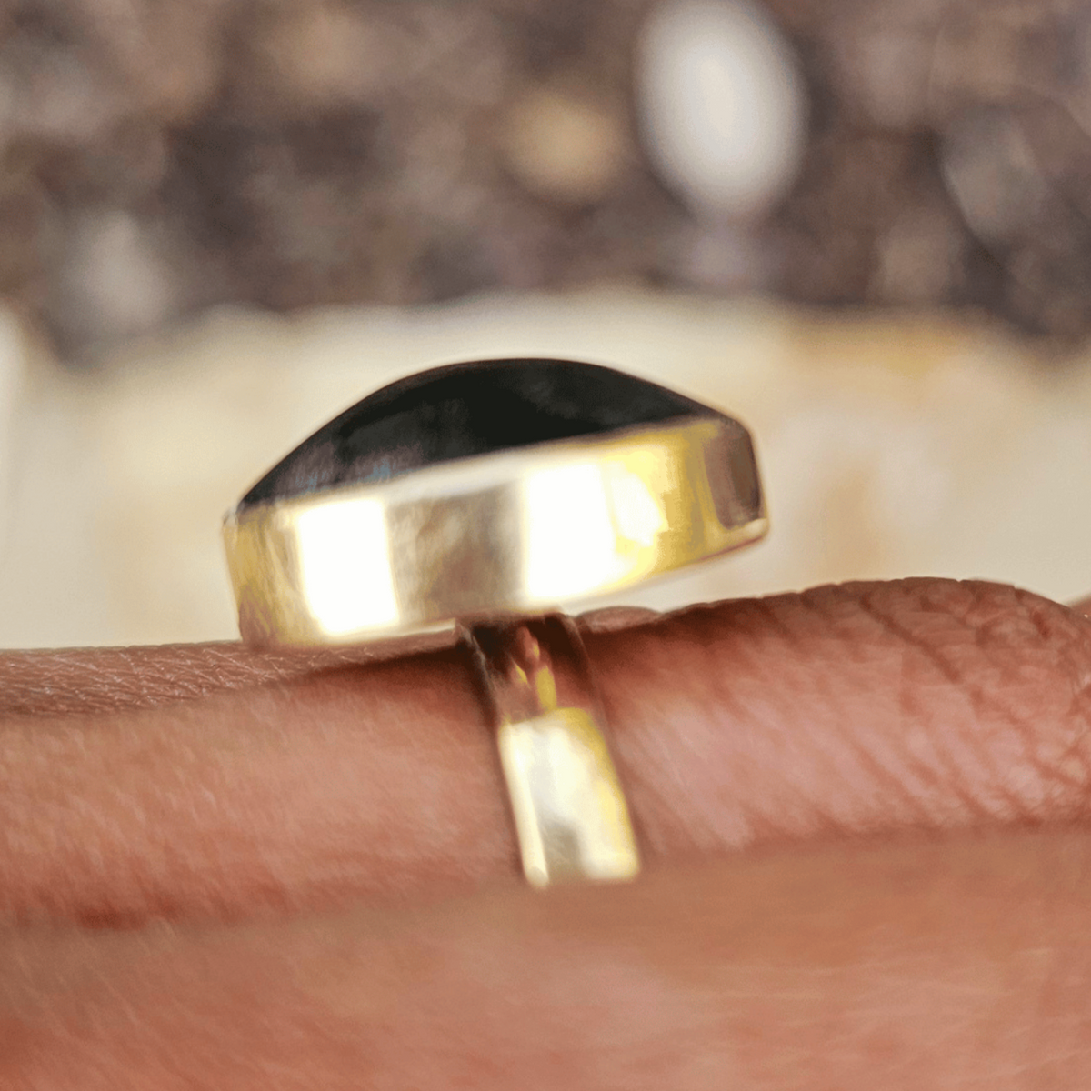 A close-up of a gold ring with a large, polished black dome stone worn on a person's finger. Shop Kamawe