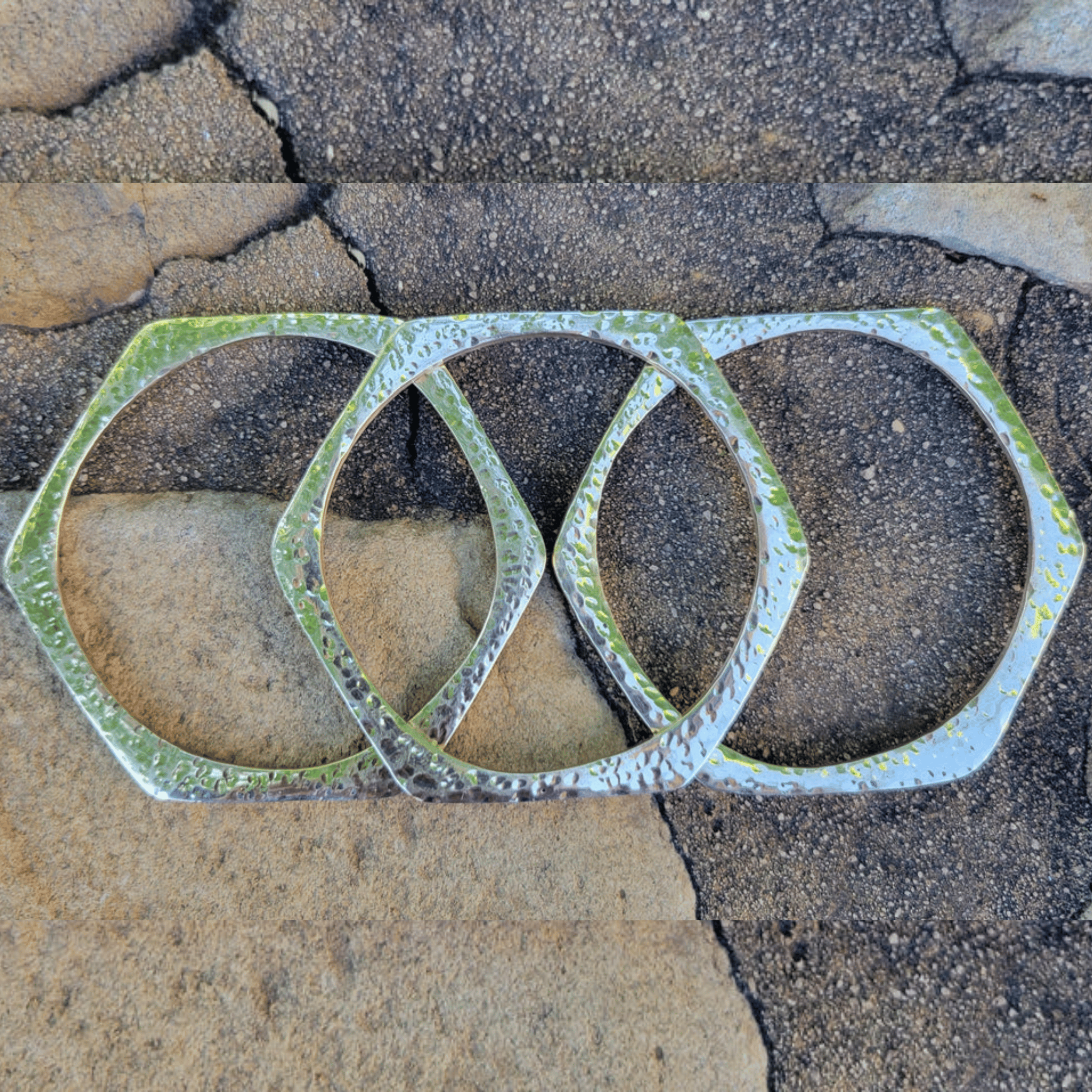 Three interlocking hammered metal rings in a hexagonal design, shown on a cracked stone surface. Shop Kamawe