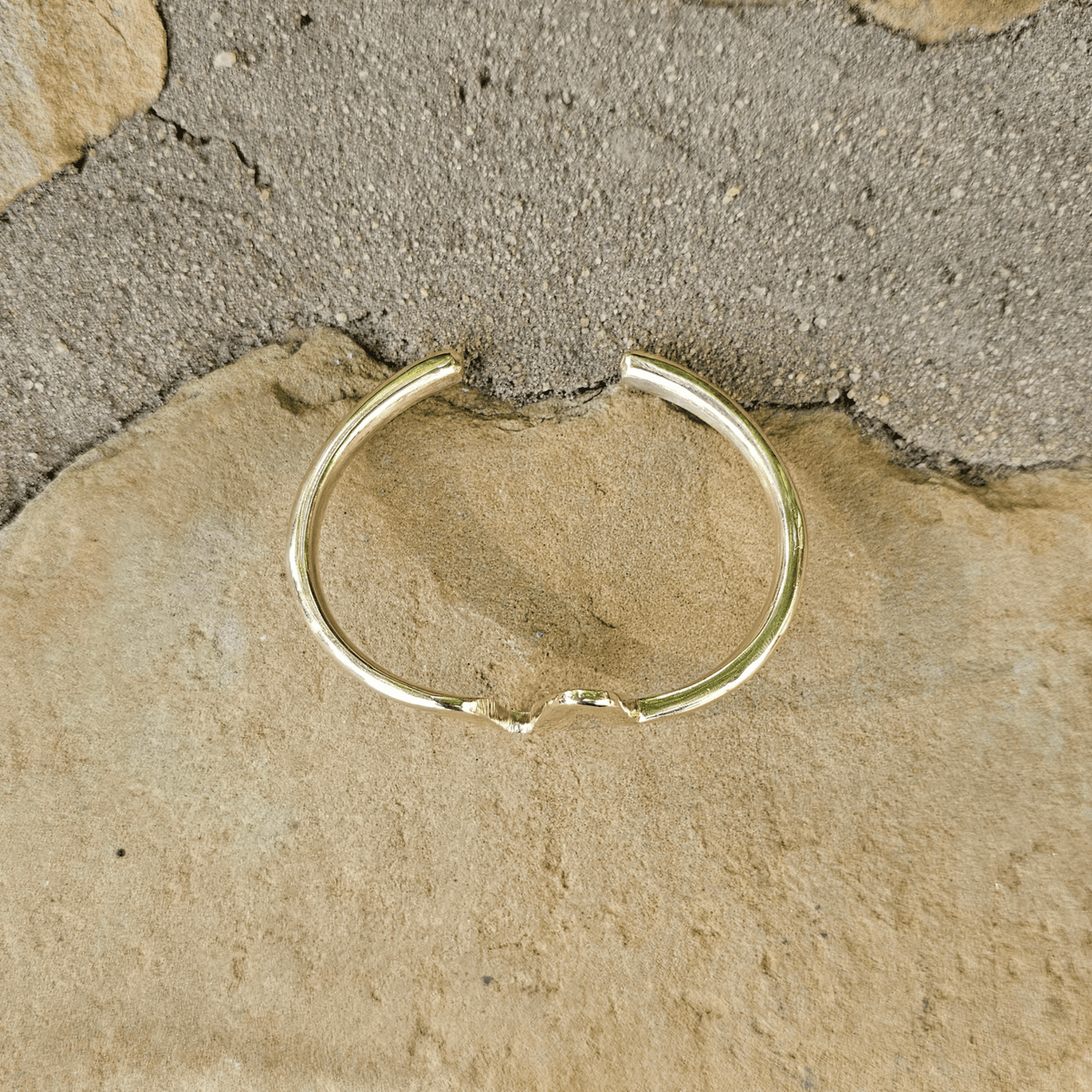 A thin gold open hoop ring, also known as a bypass ring, resting on a textured surface of beige stone. Shop Kamawe