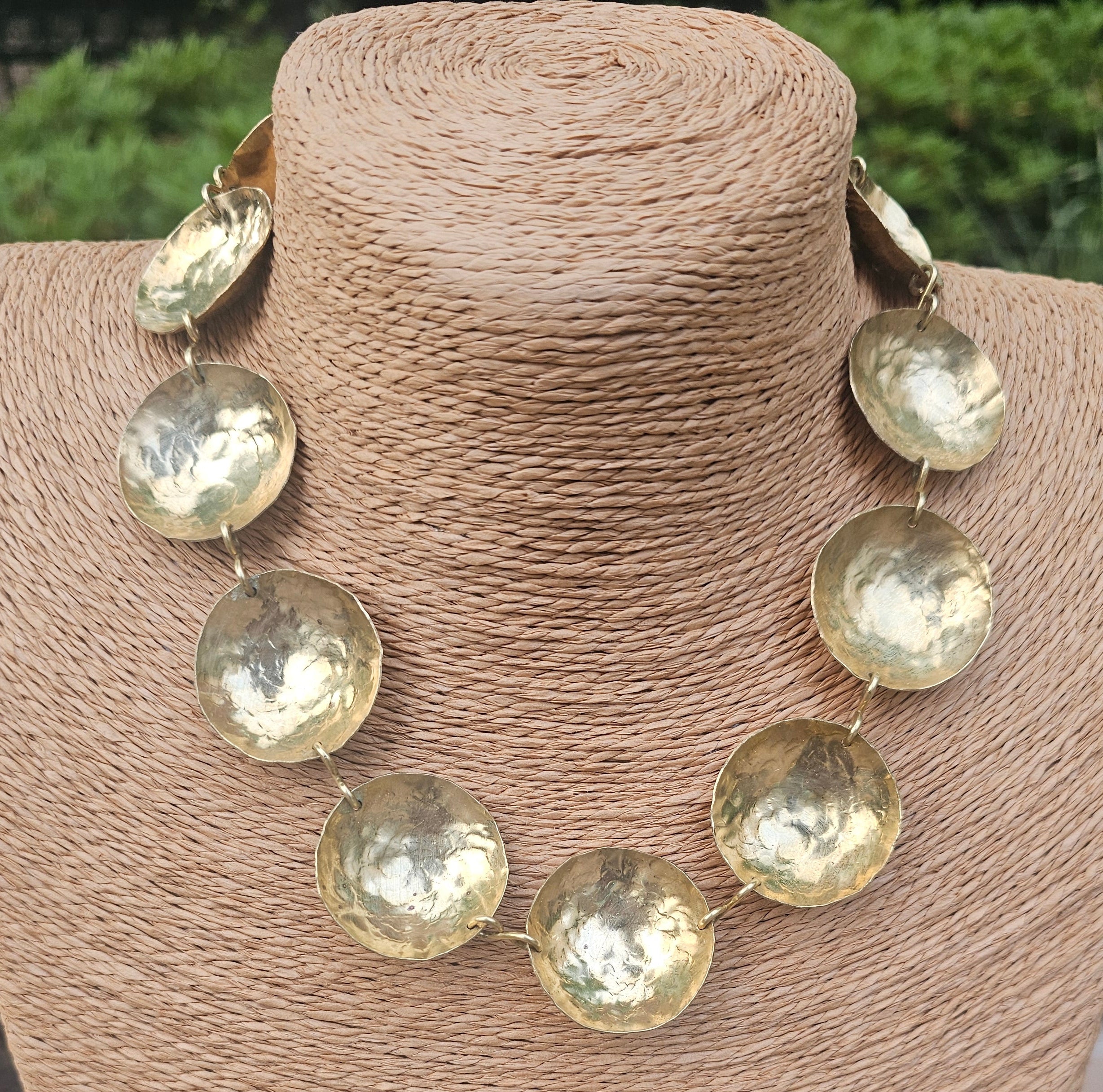 Brass necklace made of brass disc on a beige cylindrical stand with a blurred natural background