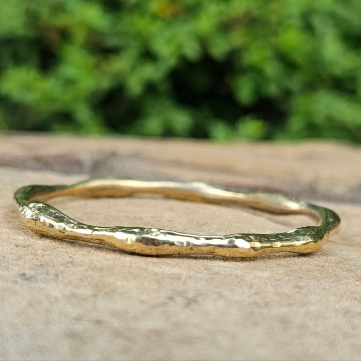 An image of gold-color Bold hammered brass bangle with wave-like texture. Shop Kamawe