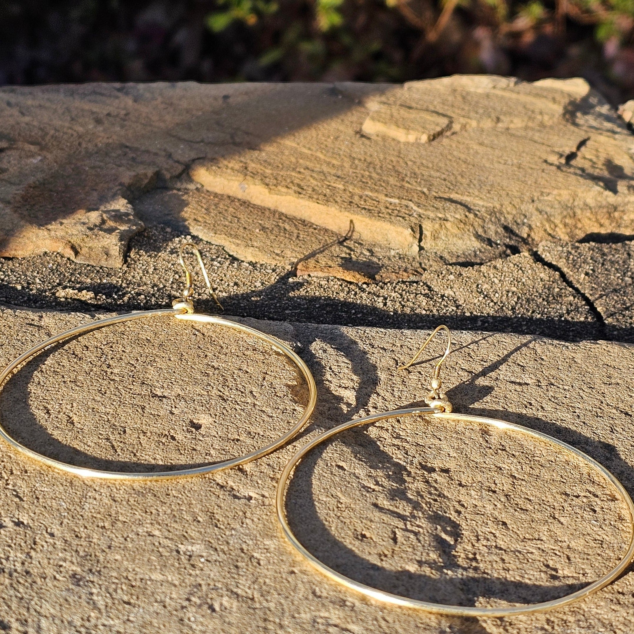 An image of gold-color Everyday mid-size polished brass hoops. Shop Kamawe