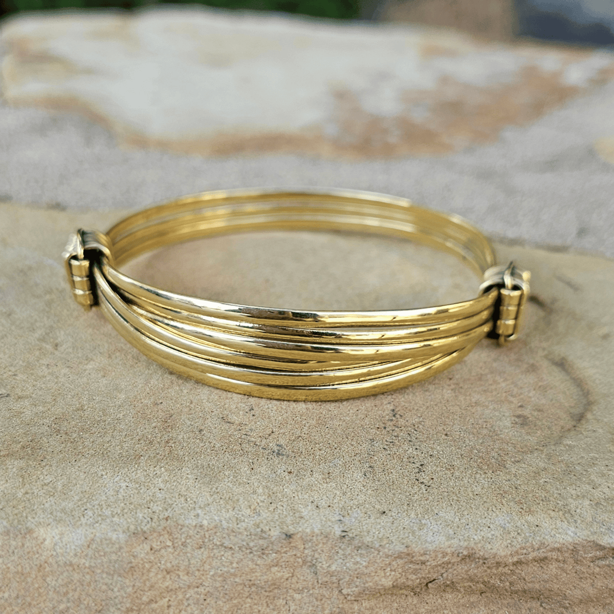 A gold-plated multi-strand bangle bracelet resting on a textured stone surface. Shop Kamawe