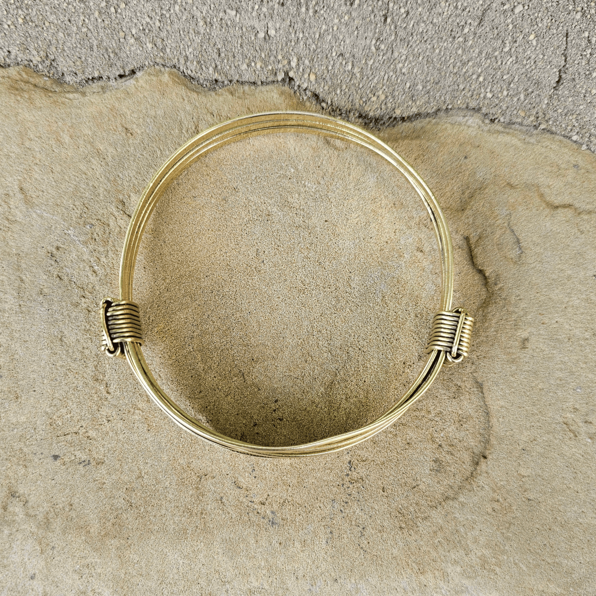 A gold-plated multi-strand bangle bracelet resting on a textured stone surface background. Shop Kamawe