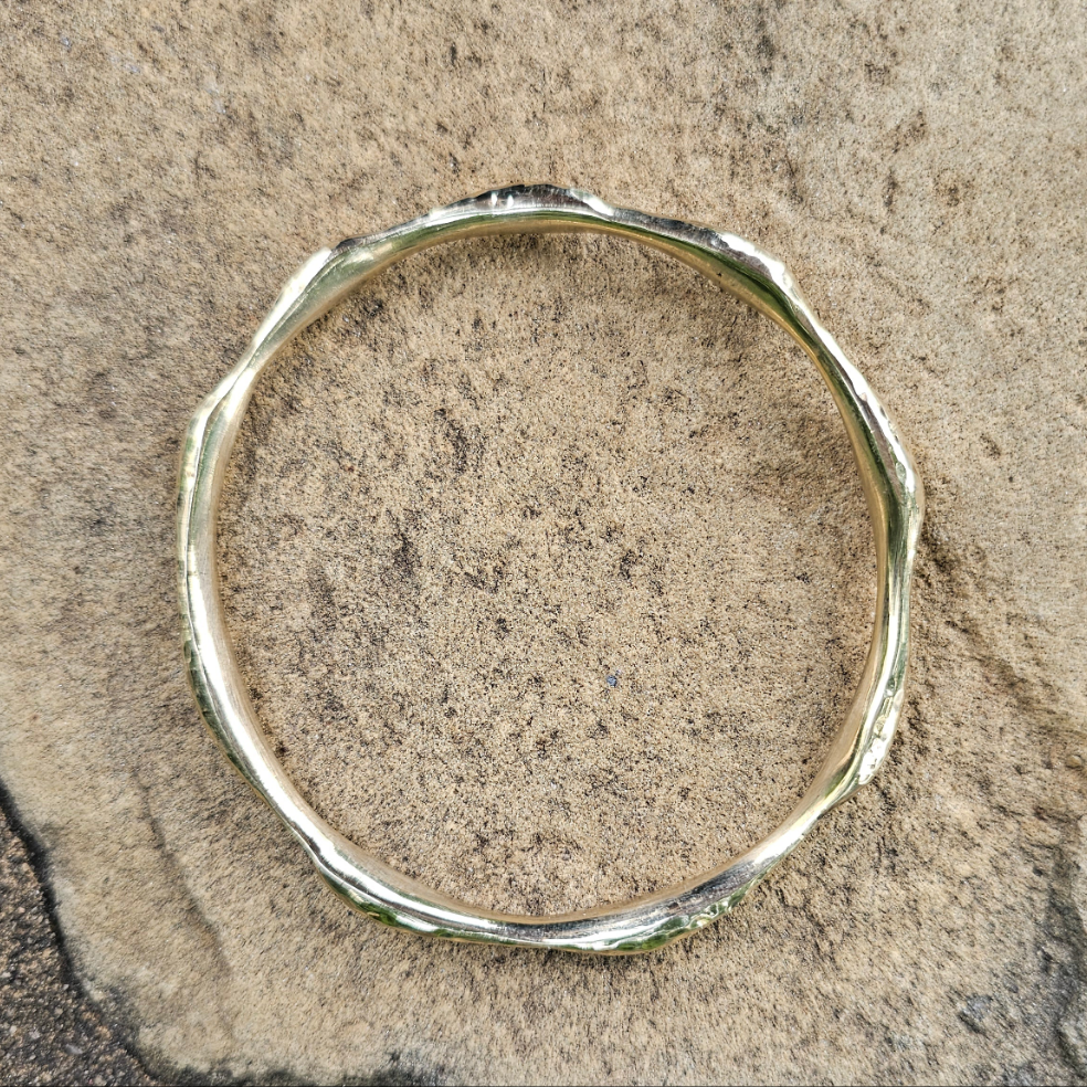 An image of gold-color Compact hammered brass bangle inspired by ocean ripples. Shop Kamawe