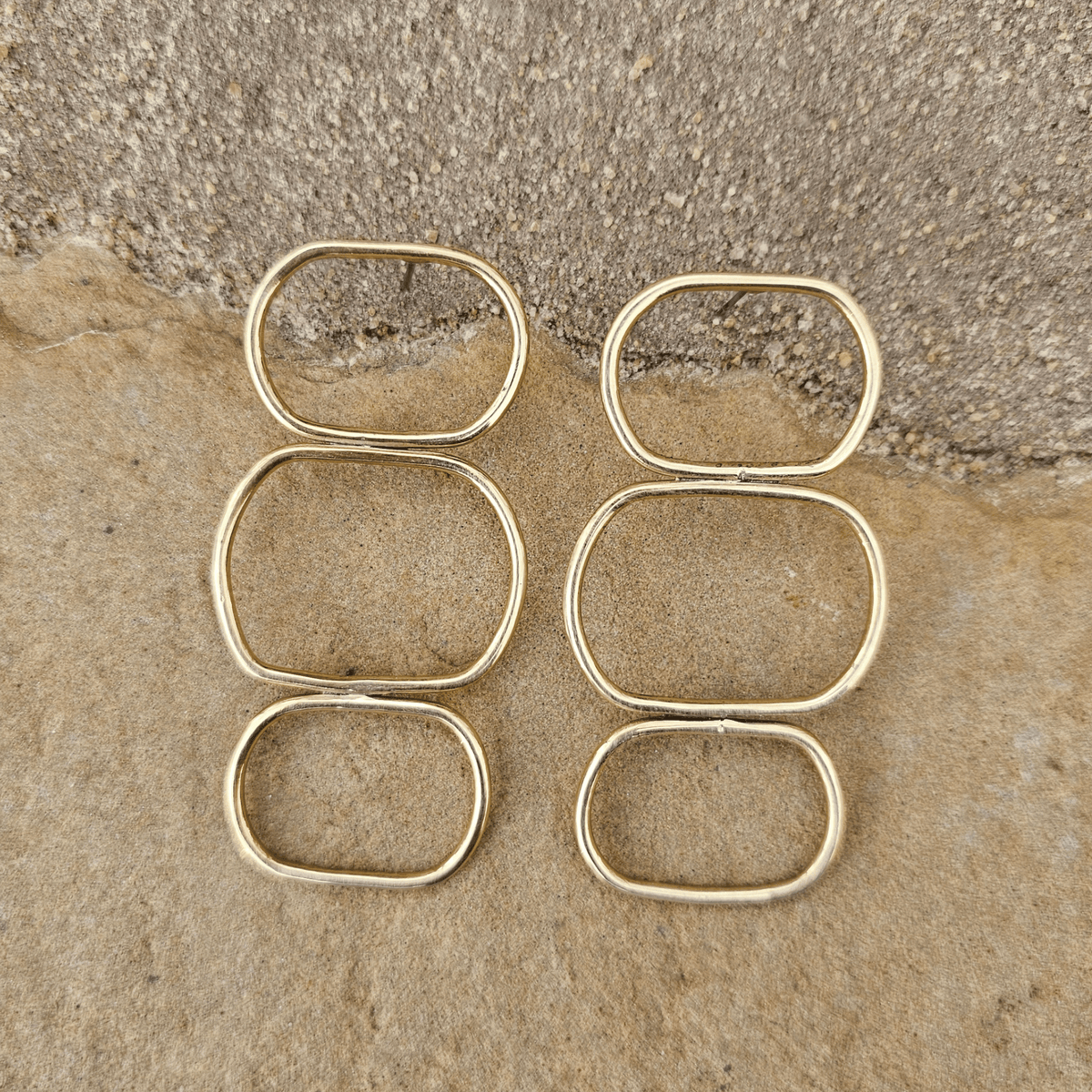 Six gold-toned metal ring clips arranged in two columns of three on a textured beige stone surface. Shop kamawe